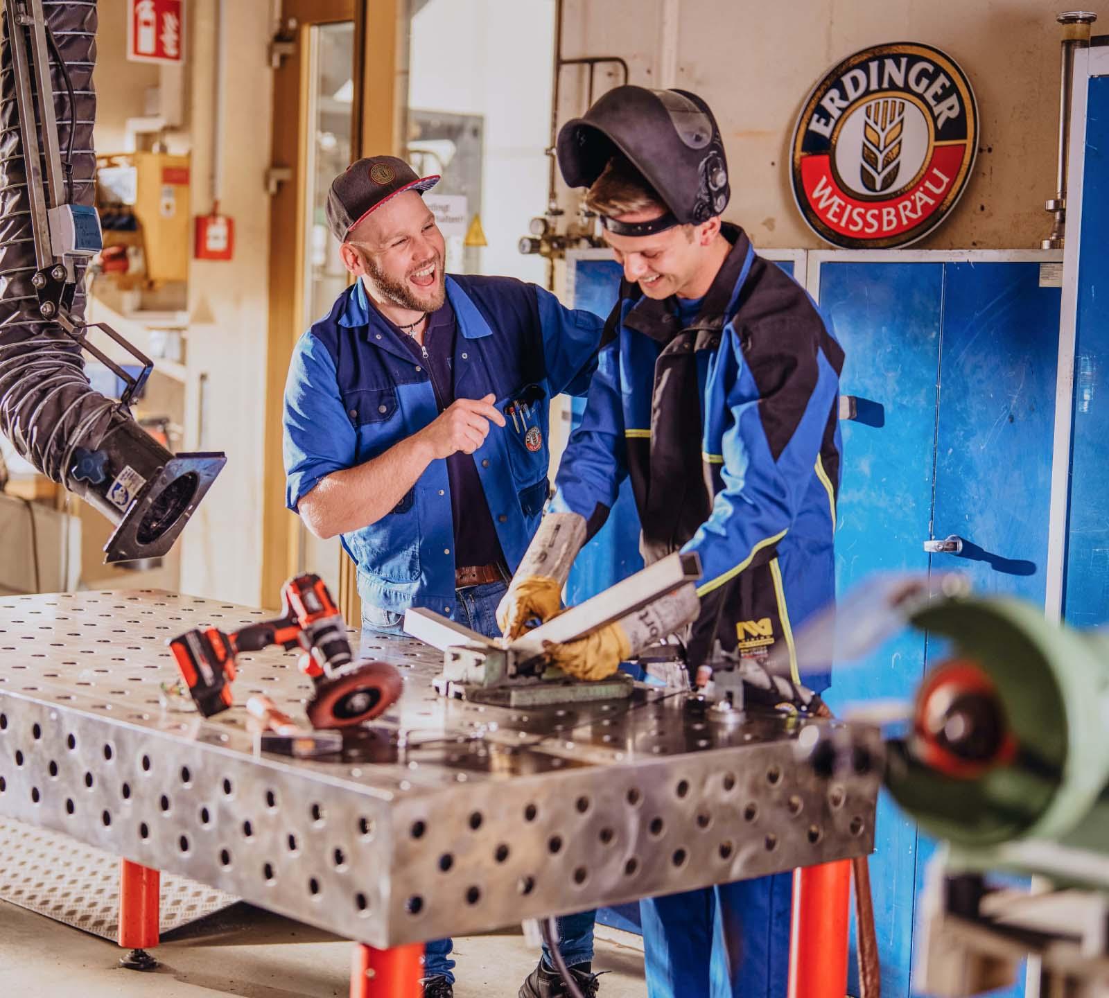 Zwei ERDINGER Industriemechaniker im Gespräch vor einer Werkbank.
