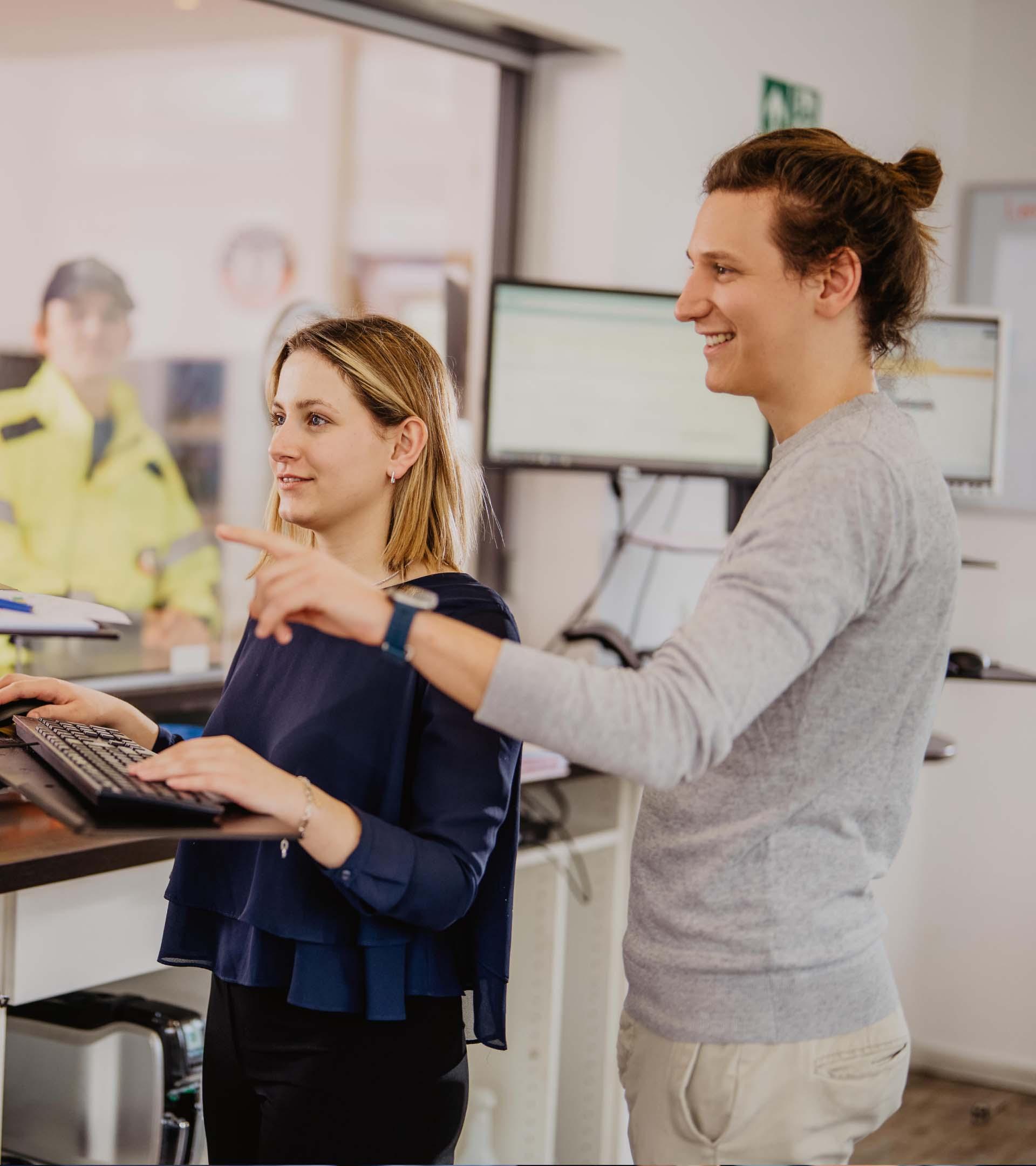 Ein ERDINGER Speditionskaufmann zeigt einer Auszubildenden etwas auf einem Monitor.